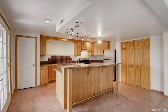 kitchen with appliances with stainless steel finishes, dark stone countertops, light tile patterned floors, a kitchen bar, and a center island with sink