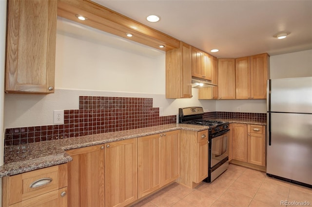 kitchen featuring freestanding refrigerator, gas range, under cabinet range hood, stone counters, and light brown cabinetry