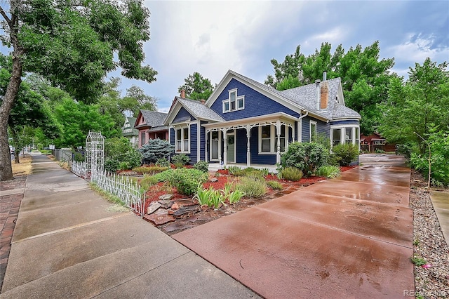 view of front of property with a shingled roof, concrete driveway, a chimney, and fence