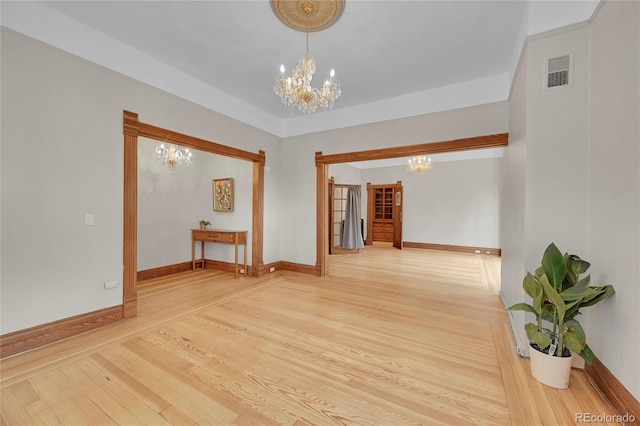 spare room with an inviting chandelier, wood finished floors, visible vents, and baseboards