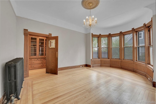 interior space featuring light wood-type flooring, baseboards, a notable chandelier, and radiator heating unit