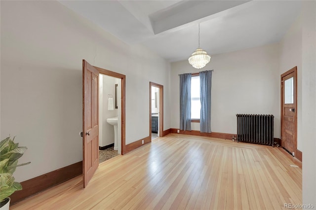 unfurnished room featuring baseboards, a notable chandelier, light wood-style flooring, and radiator heating unit