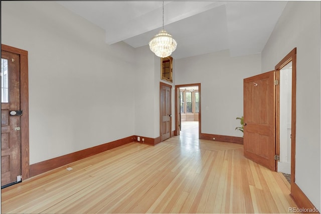 empty room with beam ceiling, a notable chandelier, wood finished floors, and baseboards