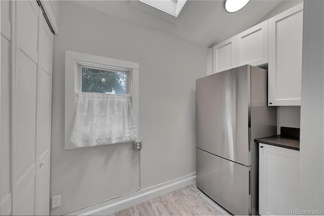 kitchen featuring dark countertops, baseboards, freestanding refrigerator, light wood-style floors, and white cabinetry