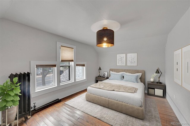 bedroom with radiator, baseboards, lofted ceiling, and hardwood / wood-style flooring