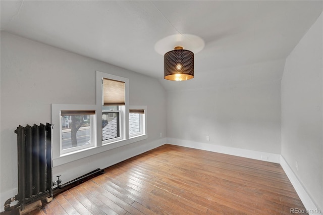 unfurnished room with vaulted ceiling, radiator, baseboards, and hardwood / wood-style flooring