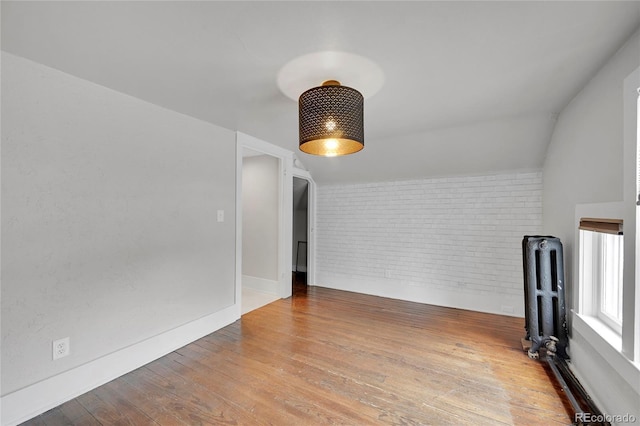 unfurnished room with hardwood / wood-style flooring, radiator heating unit, baseboards, and brick wall