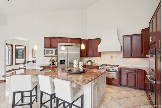 kitchen with arched walkways, built in appliances, custom exhaust hood, and high vaulted ceiling