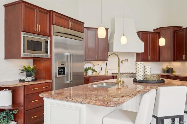 kitchen featuring built in appliances, custom exhaust hood, tasteful backsplash, light stone counters, and decorative light fixtures