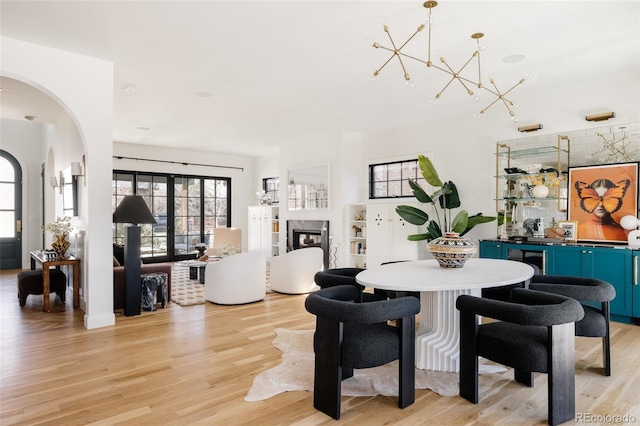 dining area with light wood-style flooring, arched walkways, a chandelier, and a glass covered fireplace