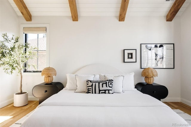 bedroom featuring baseboards, wood finished floors, and beamed ceiling