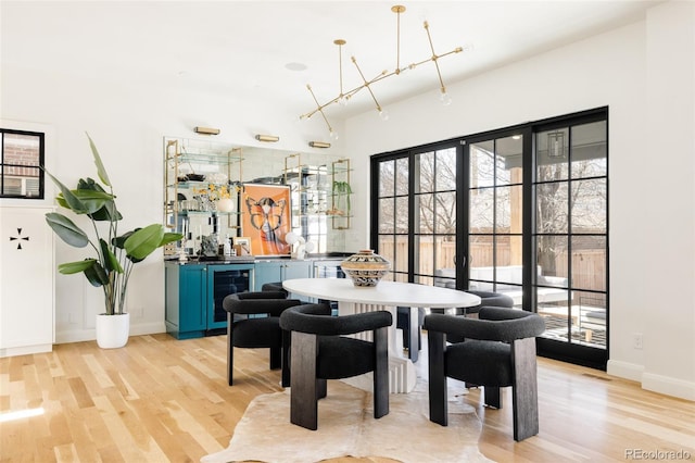 dining space featuring beverage cooler, indoor bar, baseboards, and light wood-style floors