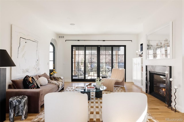 living area with light wood-style floors, baseboards, visible vents, and a high end fireplace