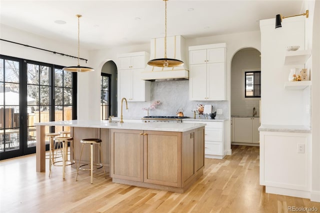 kitchen featuring light wood-type flooring, tasteful backsplash, arched walkways, and a sink