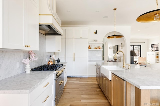 kitchen featuring arched walkways, a sink, light wood-style floors, high end stainless steel range oven, and open shelves