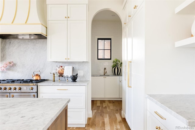 kitchen featuring white cabinetry, custom range hood, light stone counters, and stainless steel stove