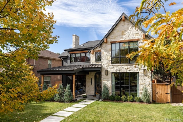 view of front of house featuring a standing seam roof, stone siding, a chimney, and a front lawn