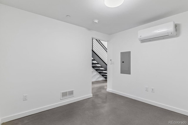 unfurnished room featuring electric panel, a wall mounted air conditioner, concrete flooring, visible vents, and baseboards
