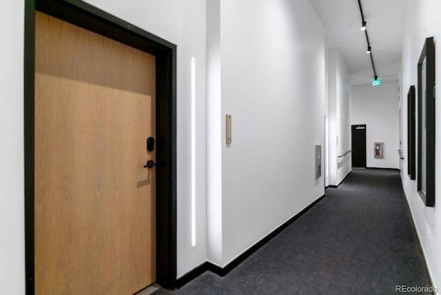 hall featuring rail lighting, baseboards, and dark carpet