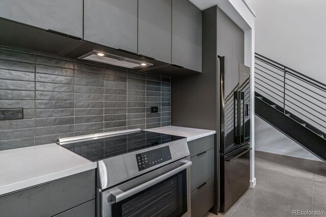 kitchen with stainless steel range with electric stovetop, freestanding refrigerator, gray cabinets, light countertops, and tasteful backsplash