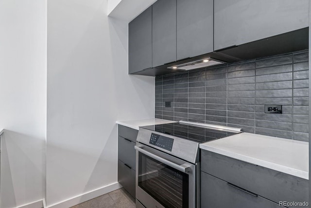 kitchen with gray cabinets, stainless steel electric range, backsplash, light countertops, and baseboards