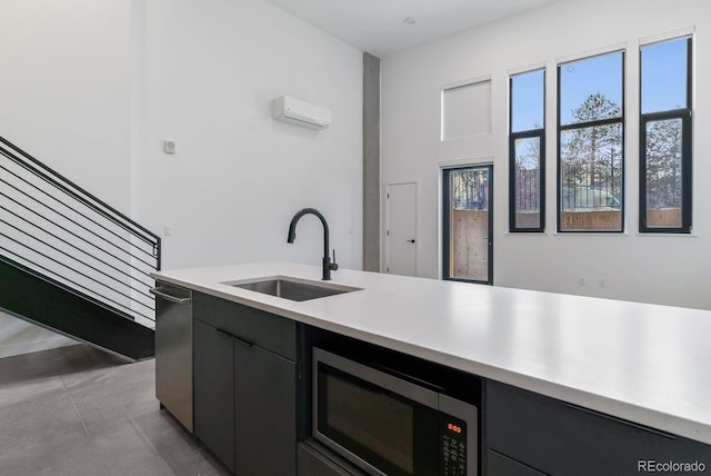 kitchen with a wall unit AC, dark cabinetry, a sink, light countertops, and appliances with stainless steel finishes
