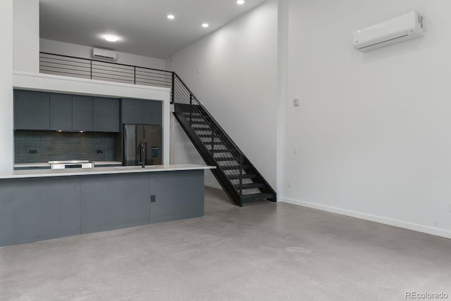 unfurnished living room with a wall mounted air conditioner, recessed lighting, baseboards, stairs, and concrete flooring
