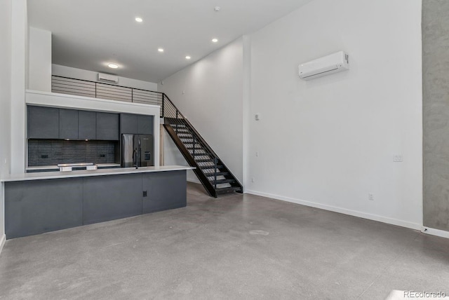 unfurnished living room featuring stairs, recessed lighting, an AC wall unit, finished concrete flooring, and baseboards