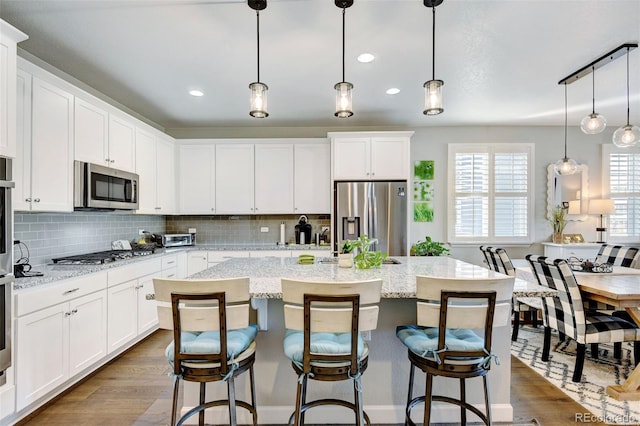 kitchen featuring hanging light fixtures, stainless steel appliances, dark hardwood / wood-style flooring, white cabinetry, and an island with sink