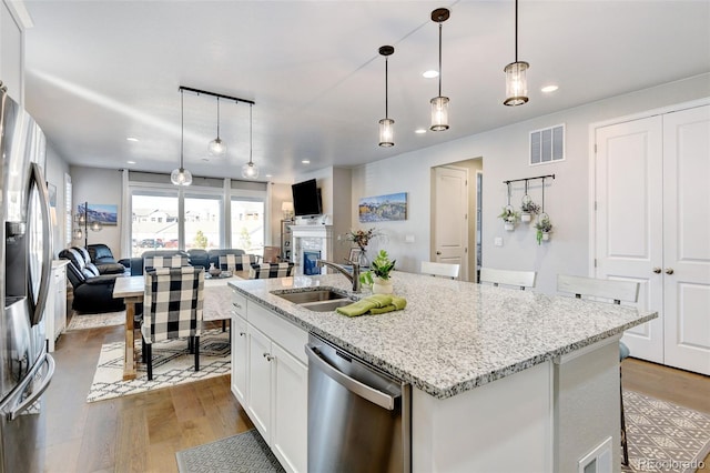 kitchen featuring light hardwood / wood-style flooring, appliances with stainless steel finishes, sink, an island with sink, and pendant lighting