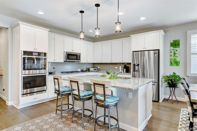 kitchen with a center island with sink, stainless steel appliances, light stone counters, and light wood-type flooring