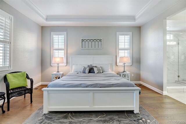 bedroom with multiple windows, a raised ceiling, ensuite bathroom, and hardwood / wood-style flooring