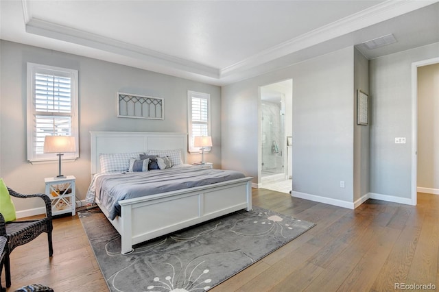 bedroom featuring crown molding, a tray ceiling, ensuite bathroom, and hardwood / wood-style flooring