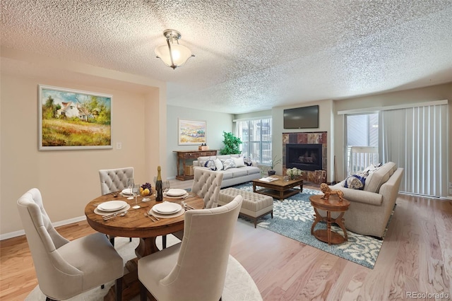 dining area featuring a tiled fireplace, a textured ceiling, wood finished floors, and baseboards