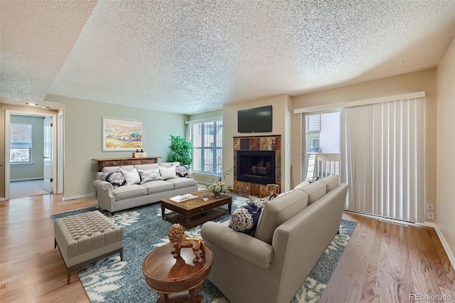 living area with a textured ceiling, light wood-style floors, a tile fireplace, and baseboards
