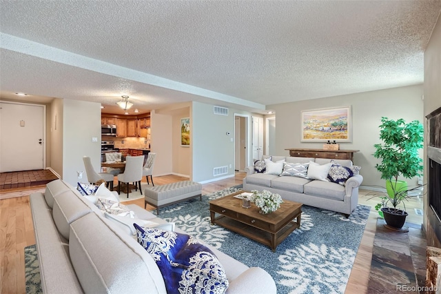living room with light wood-type flooring, a textured ceiling, baseboards, and a fireplace with flush hearth