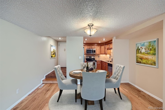 dining space featuring light wood-type flooring, baseboards, a textured ceiling, and recessed lighting