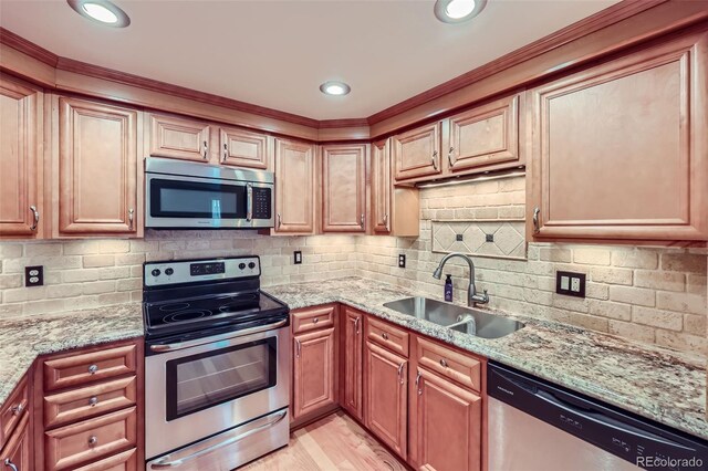 kitchen featuring appliances with stainless steel finishes, a sink, light stone countertops, decorative backsplash, and crown molding