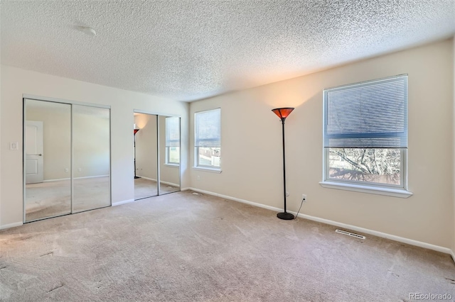 unfurnished bedroom featuring multiple closets, carpet, a textured ceiling, and baseboards