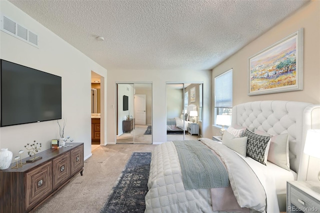 bedroom featuring light carpet, a textured ceiling, multiple closets, and ensuite bathroom