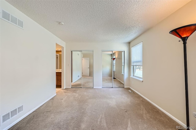 unfurnished bedroom featuring multiple closets, carpet, a textured ceiling, and baseboards