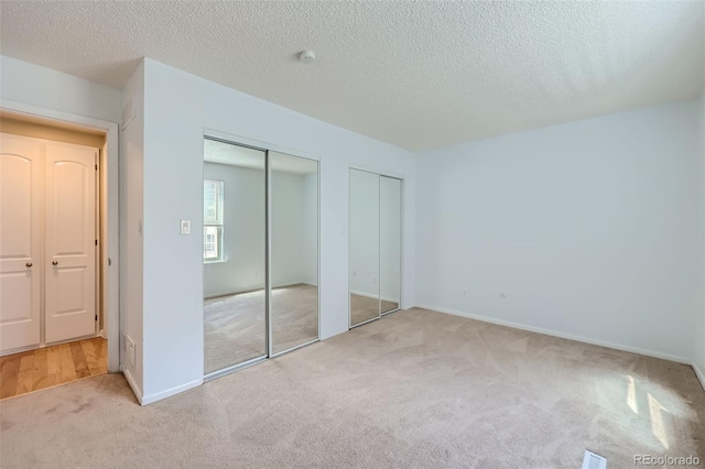 unfurnished bedroom with carpet floors, two closets, a textured ceiling, and baseboards