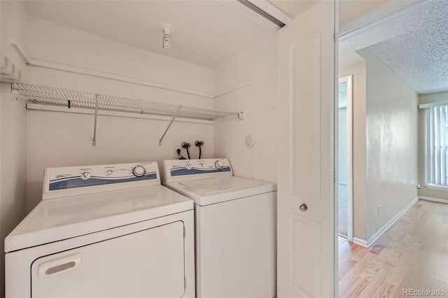 clothes washing area featuring washer and clothes dryer, light wood-style flooring, baseboards, and a textured ceiling