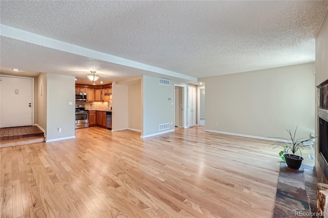 unfurnished living room featuring a textured ceiling, light wood-style floors, baseboards, a fireplace, and a sink