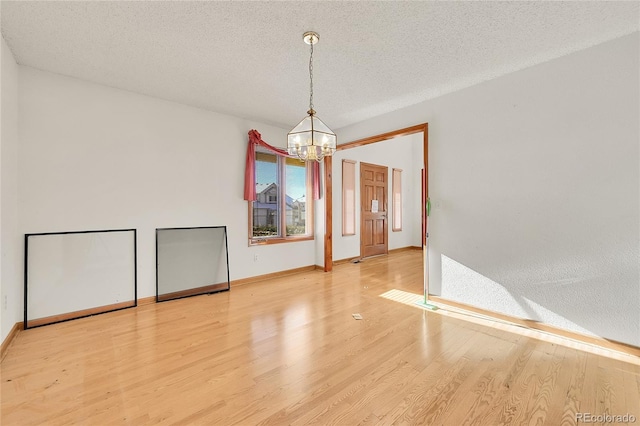 unfurnished room with light wood-type flooring, an inviting chandelier, baseboards, and a textured ceiling