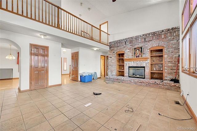 unfurnished living room with a brick fireplace, visible vents, a high ceiling, and baseboards