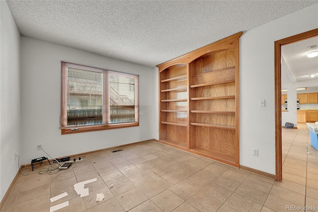 unfurnished room with a textured ceiling, baseboards, and light tile patterned floors