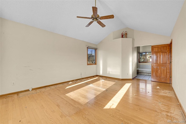 spare room with light wood-style floors, high vaulted ceiling, baseboards, and a ceiling fan