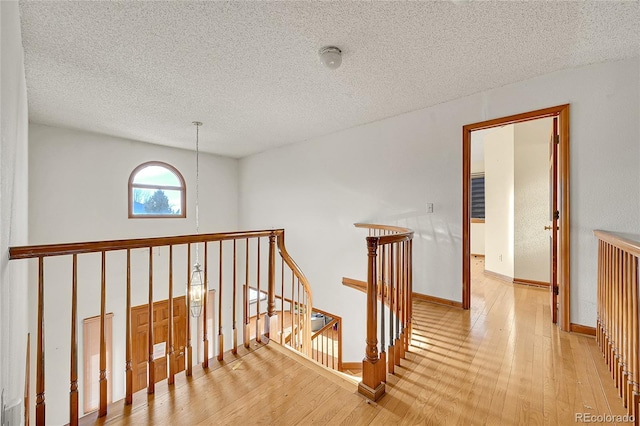 hallway featuring a textured ceiling, light wood-style flooring, an upstairs landing, and baseboards