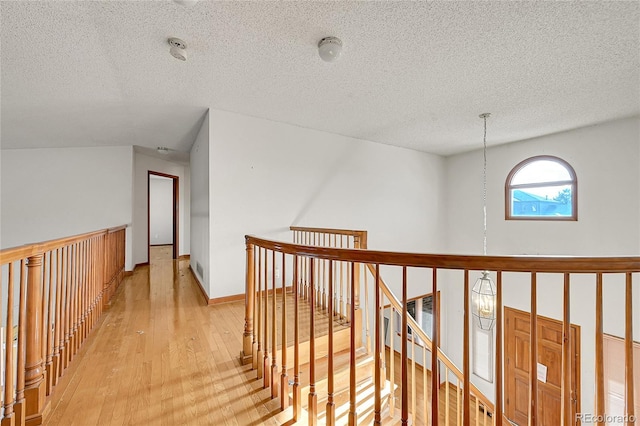 hallway with light wood-type flooring, baseboards, a textured ceiling, and an upstairs landing